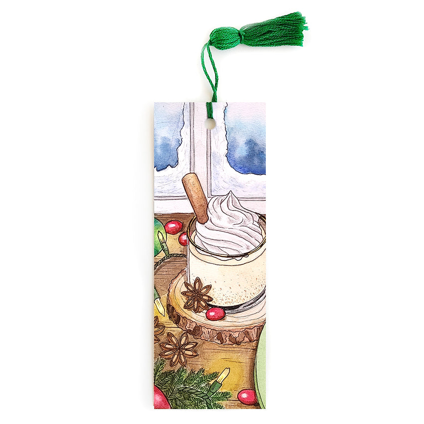 Bookmark of an eggnog drink with star anise and cinnamon with a snowy window in the background. Has a green tassel.