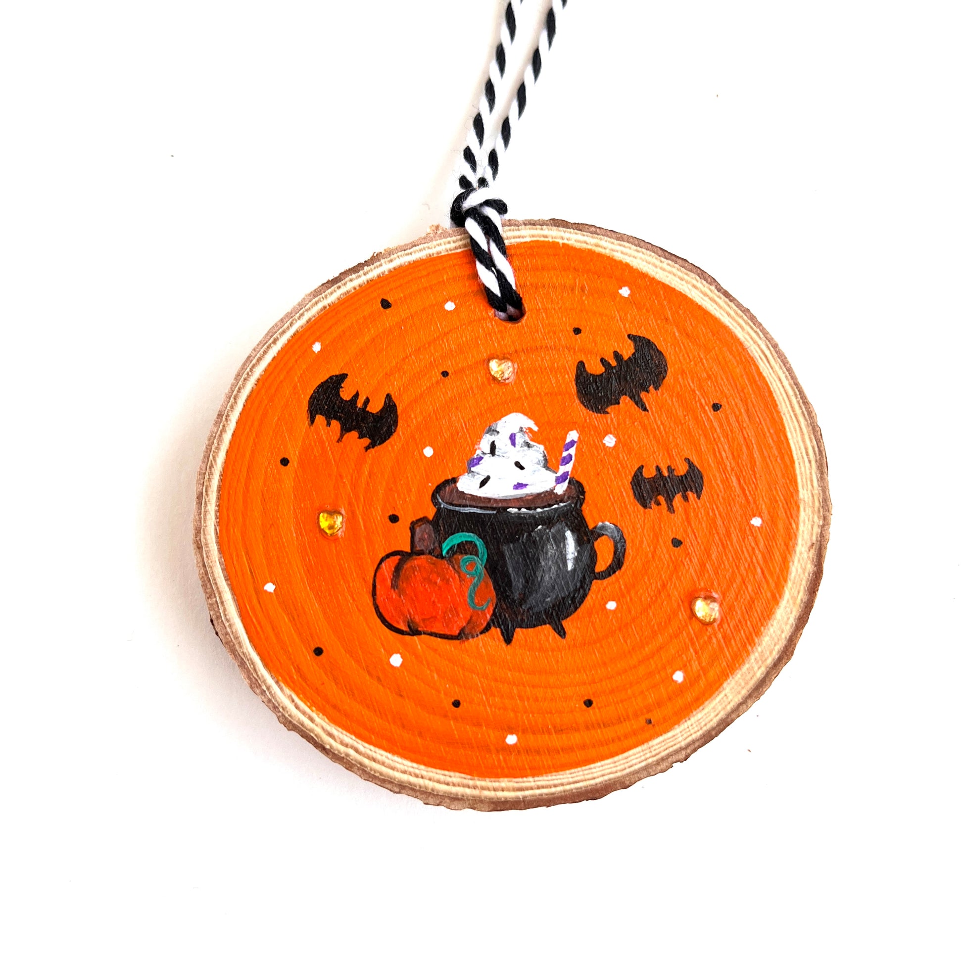 wooden ornament with halloween inspired pumpkin spice latte with bats floating around the cauldron mug. A small pumpkin sits in front of the mug and there are orange heart rhinestones decorating the background.