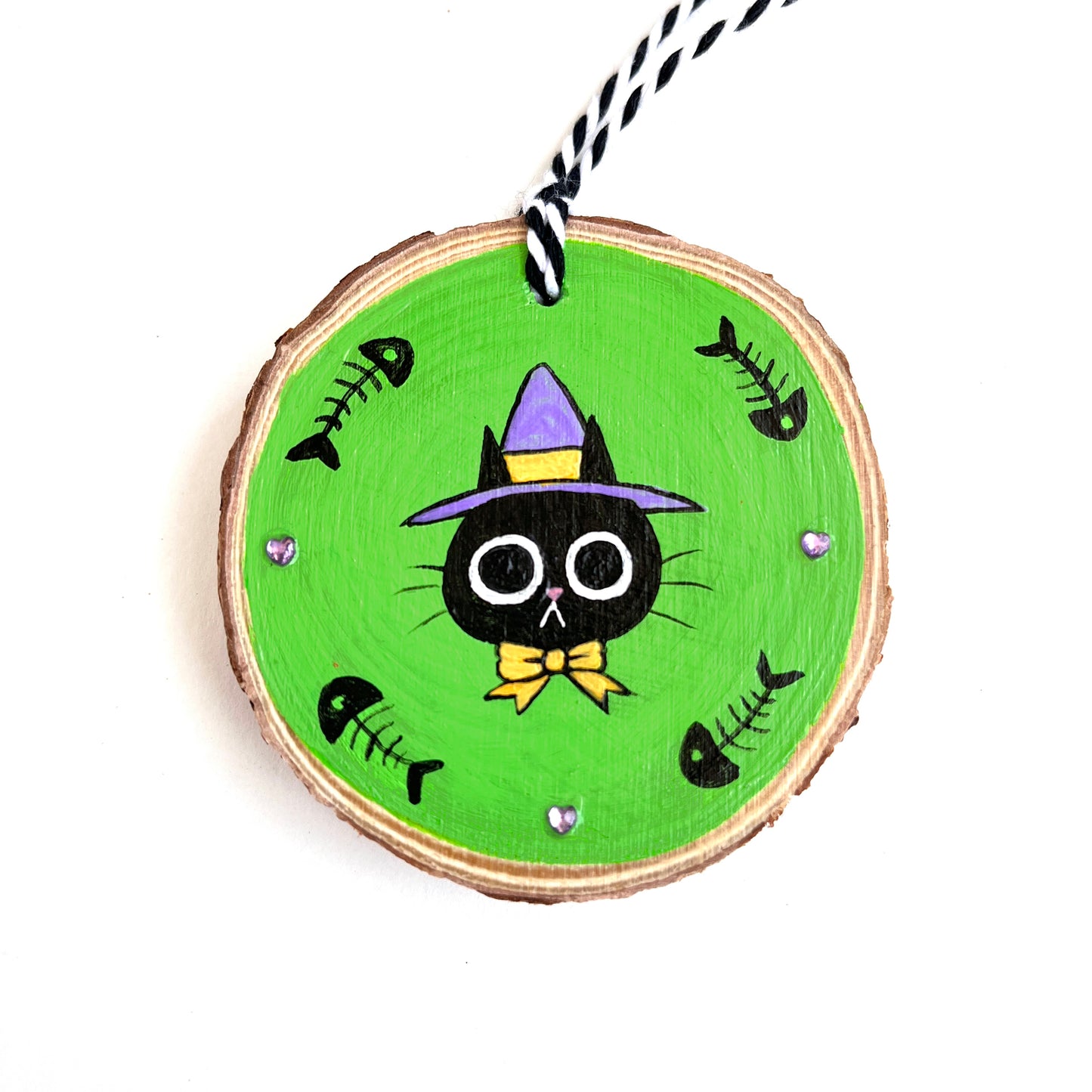 cute ornament with wide eyed black cat with a witch hat and bow with a bright green background, fishbones, and purple rhinestones