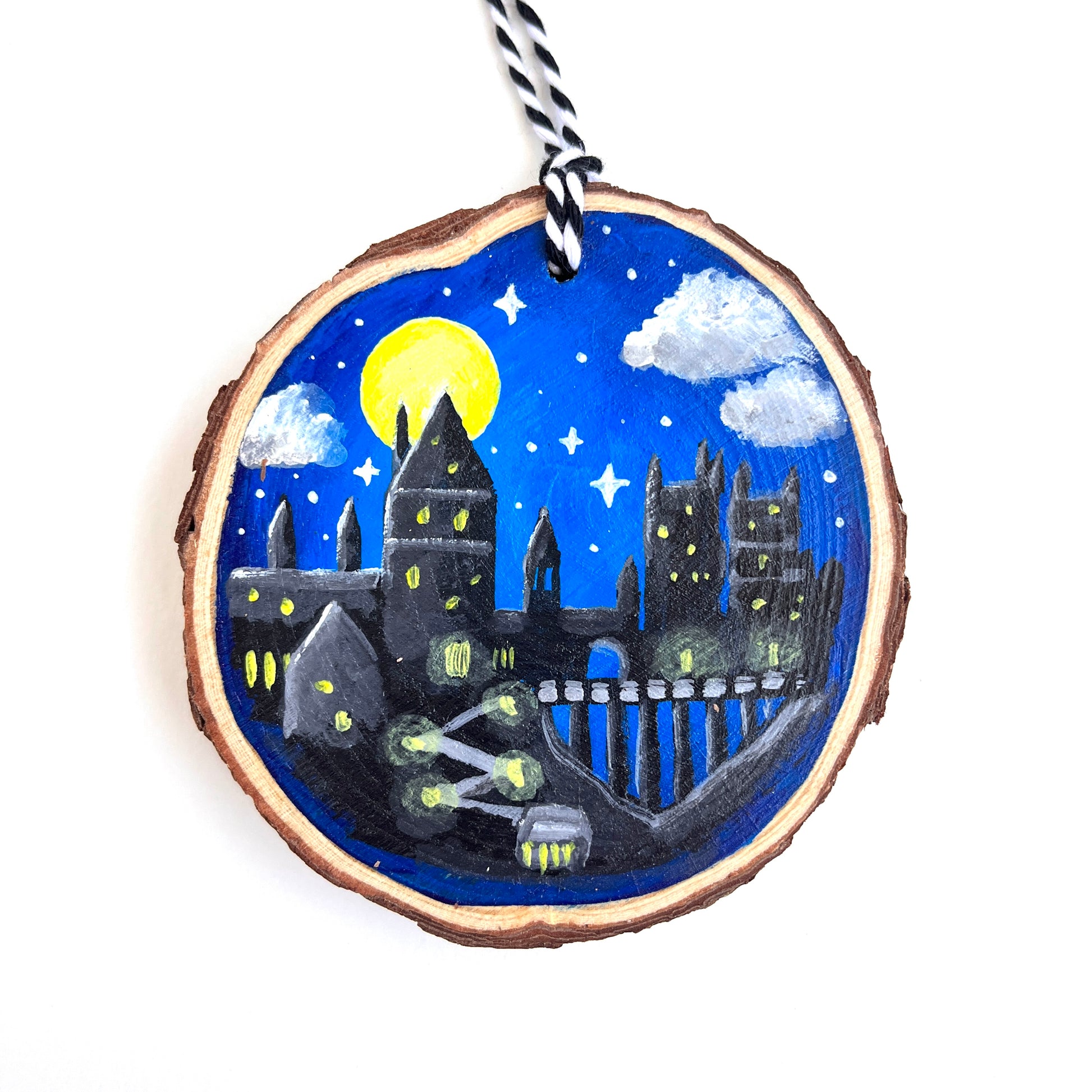 A hand painted wooden ornament of the Hogwarts castle from Harry Potter.  A full moon rises behind the Gryffindor tower.