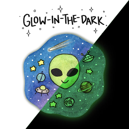 A die-cut sticker featuring a hand-drawn green alien head and outer space scene, with the text 'GLOW-IN-THE-DARK' above it. The sticker is split diagonally into blue and green glowing colors, with a black background behind it.