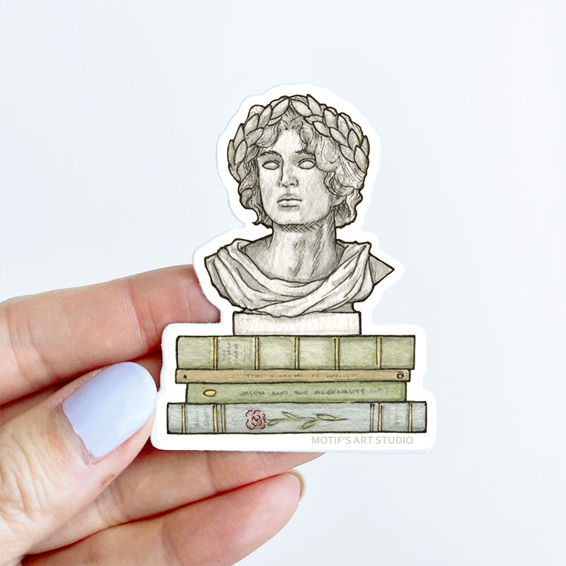 Sticker of a Greek god bust on books held by a hand for size reference.