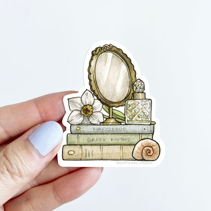 Sticker of a vintage mirror, books, and a white daffodil flower held by a hand.
