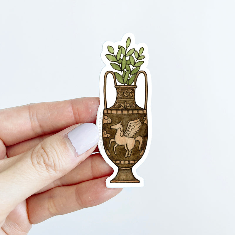 Hand holding a sticker of an ancient greek vase of Pegasus filled with ferns.