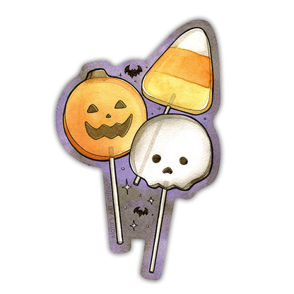A die-cut sticker featuring three cute Halloween-themed lollipops: a jack-o'-lantern, a skull, and a candy corn, set against a purple background with small black bats and white stars.