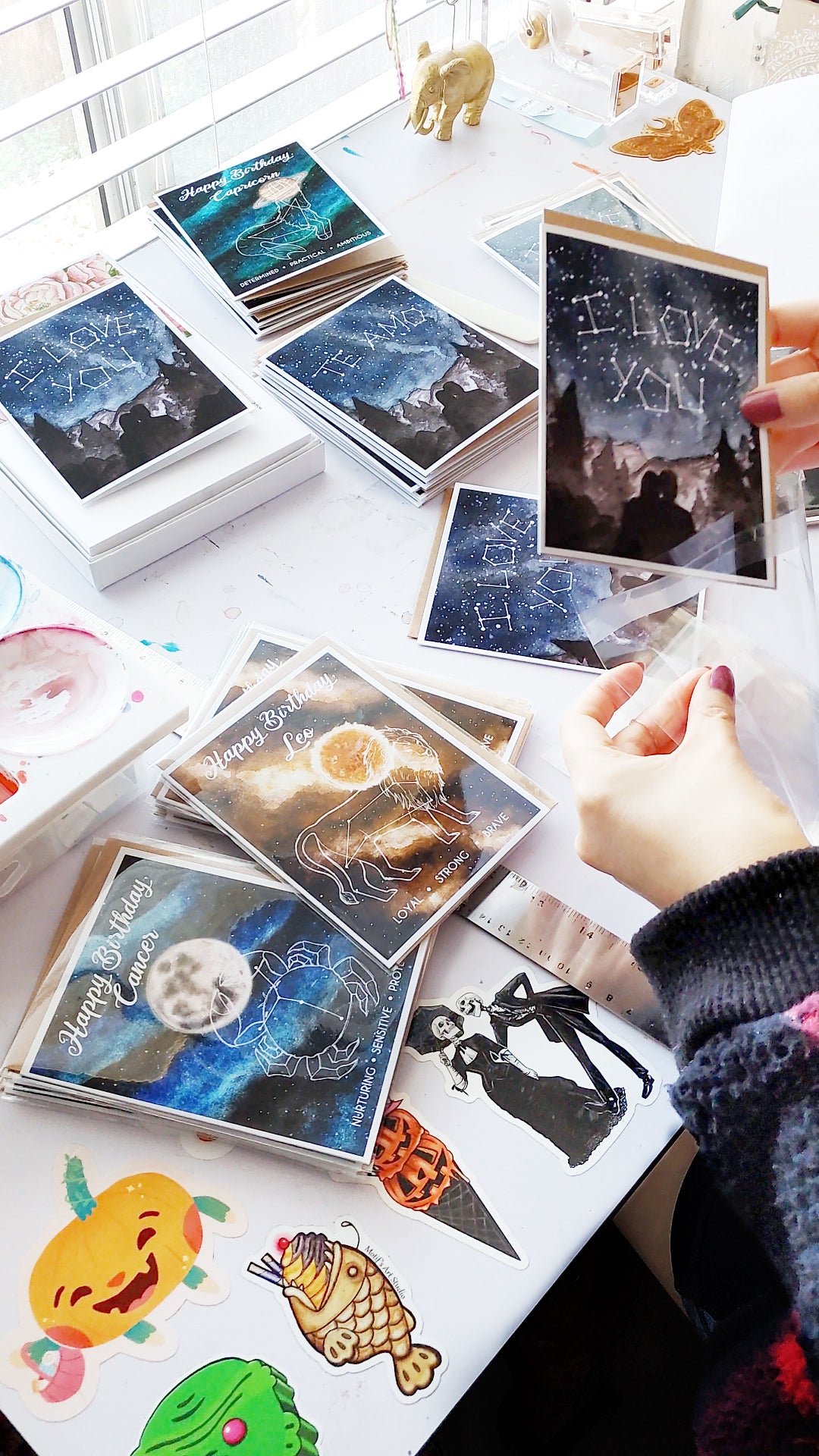 The artist at her desk packaging her a bunch of her own handmade greeting cards with envelopes and cello sleeves.
