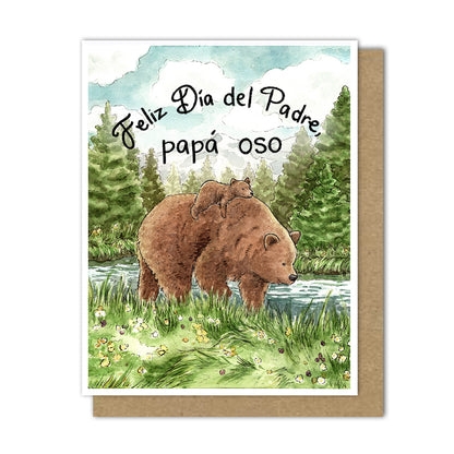 A greeting card featuring a large brown bear with a little cub on its back walking through a meadow next to a forest. It reads "Feliz Dia del Padre, papa oso"