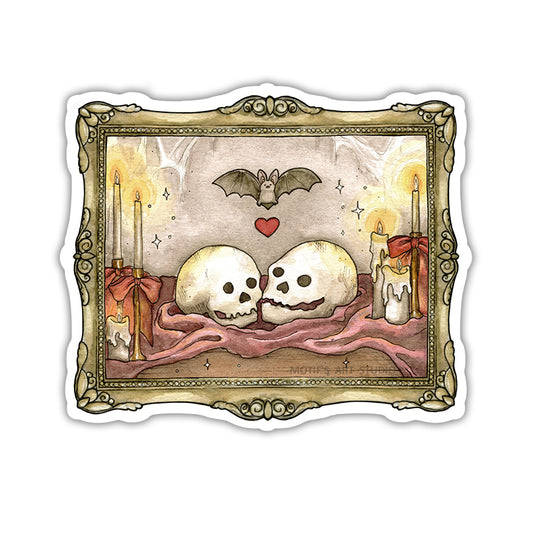A die-cut sticker featuring a gothic illustration of two skulls resting on a maroon cloth, flanked by lit candles, with a bat and a red heart above, all framed by an ornate gold frame.