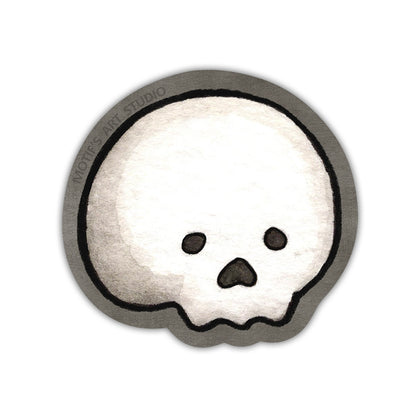 A die cut sticker of a cute white skull with a dark gray border.