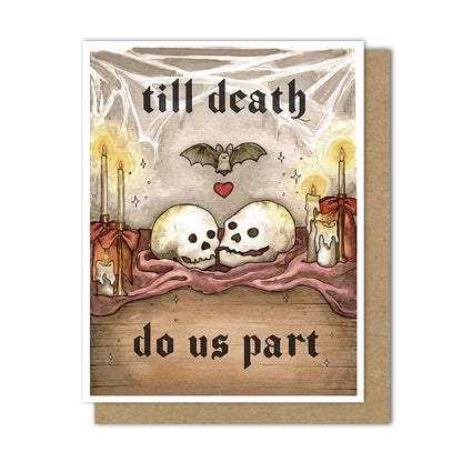 An A2 greeting card with a kraft envelope behind it. The card artwork shows two skulls resting on a maroon cloth, with candles, a bat, stars, and the gothic text 'till death do us part' in a dark, romantic setting.